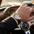Hand wearing a gold watch on a car dashboard with a Mercedes-Benz emblem.
