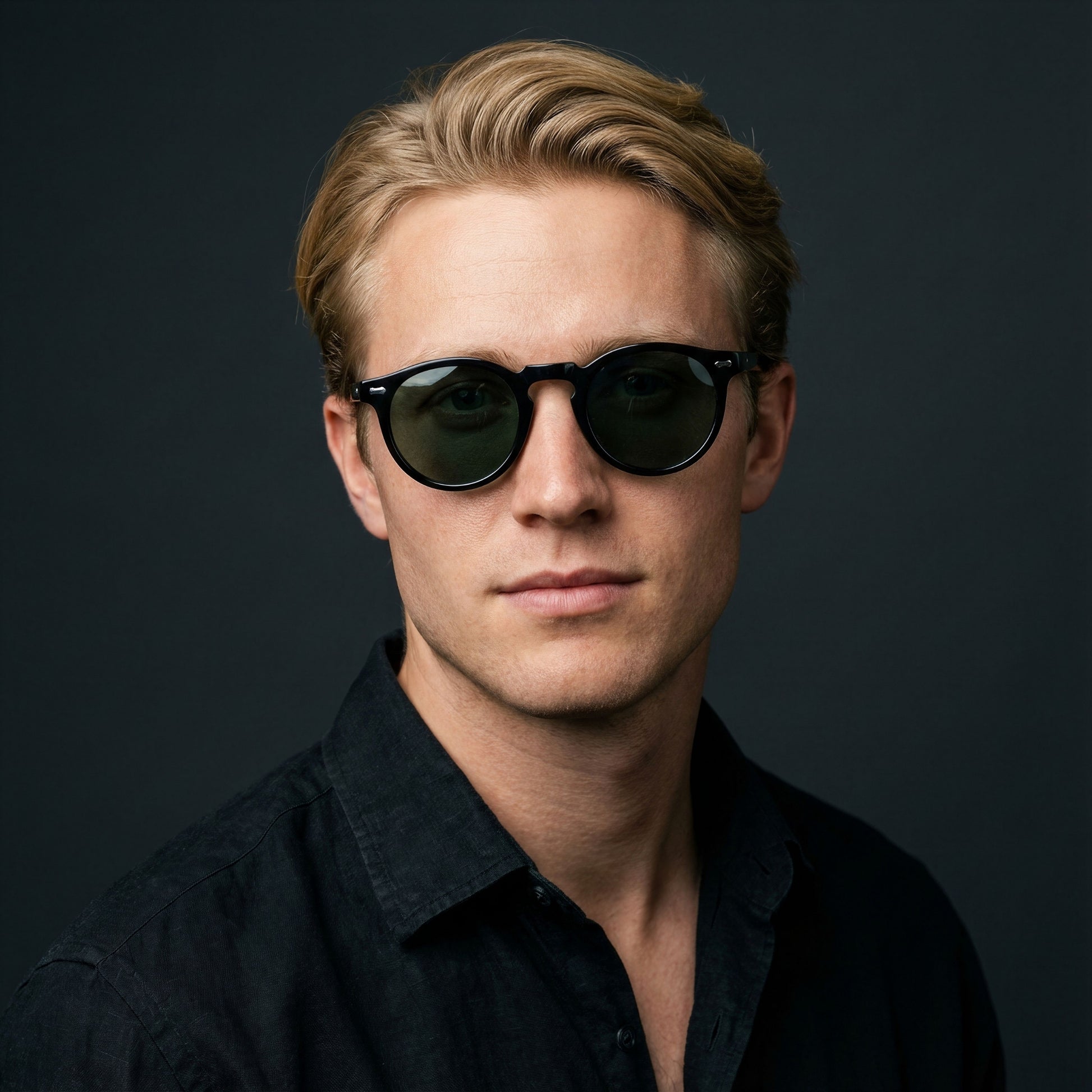 Man wearing dark sunglasses and a black shirt against a dark background