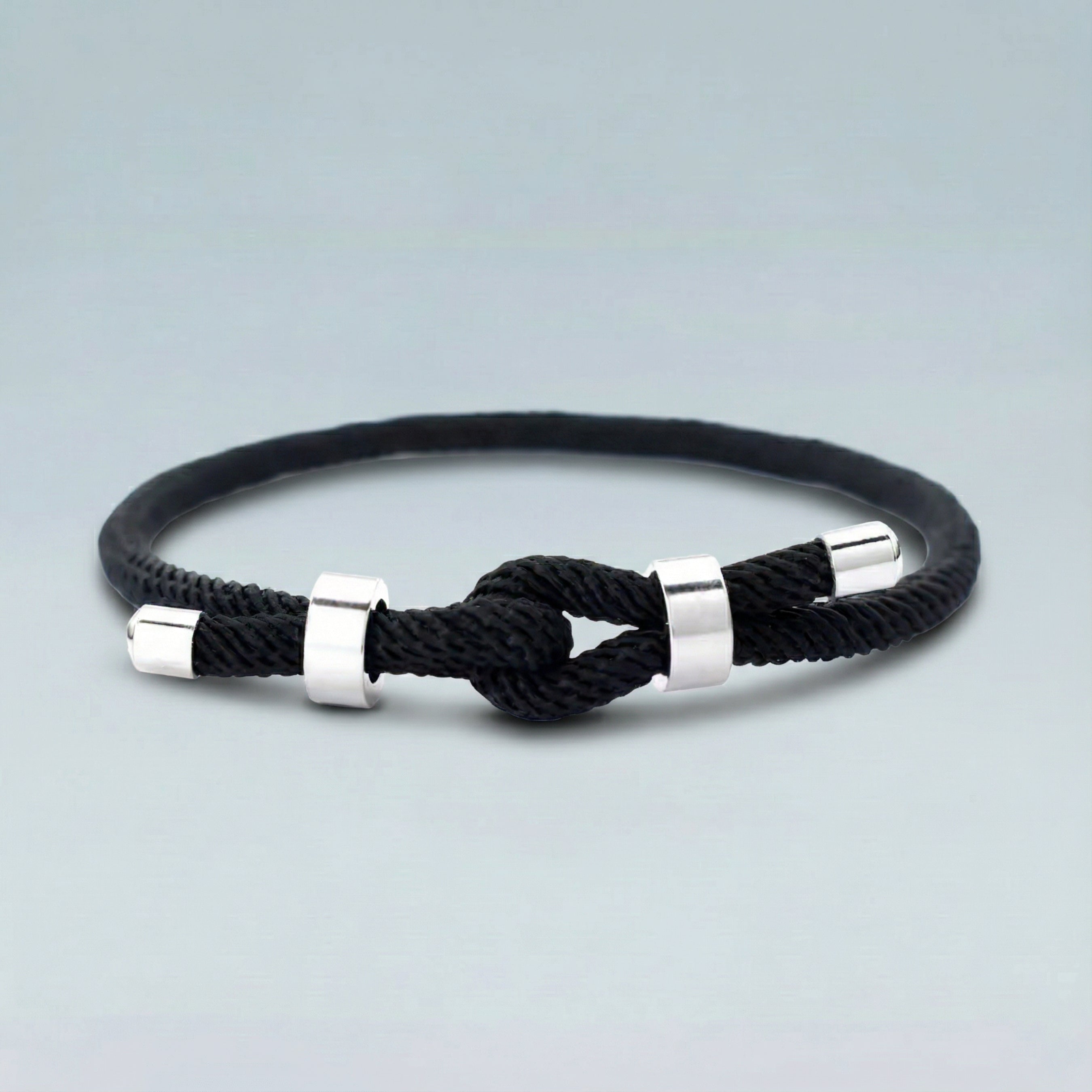 Black braided bracelet with silver knots on a light gray background