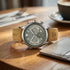Wristwatch with brown leather strap on a wooden table with a cup of coffee in the background